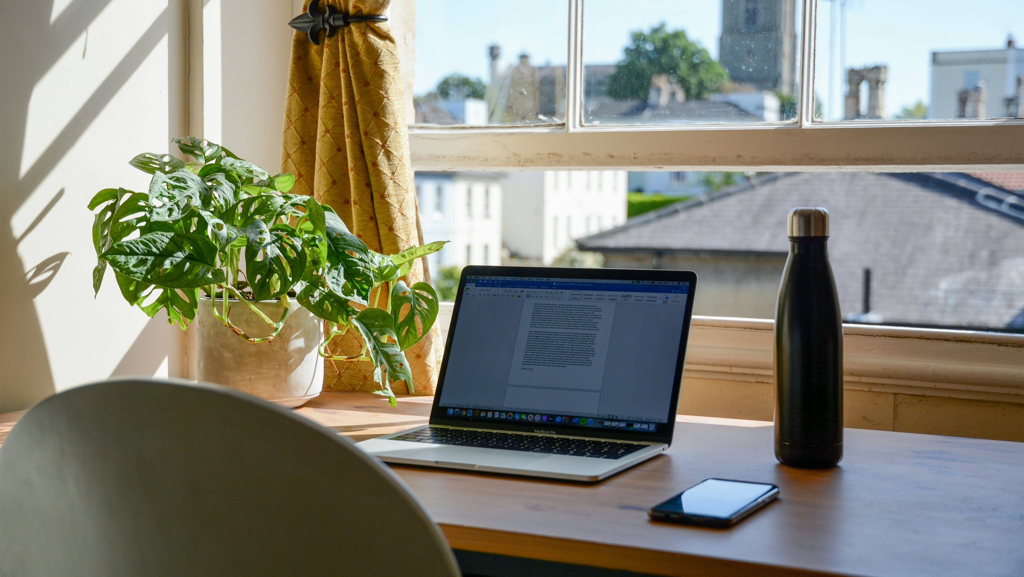 モンステラの観葉植物が置かれた窓辺のデスクでMacBook Proを使う在宅ワーク環境